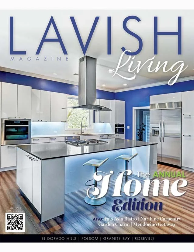 Cover of Lavish Living magazine featuring a modern kitchen with white cabinets, a large island with bar stools, stainless steel appliances, and a blue accent wall.