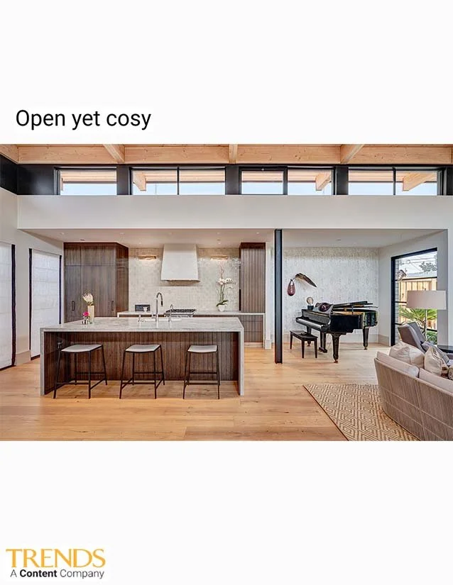 Open-concept living space with kitchen island, bar stools, grand piano, and sitting area with a sofa, featuring modern decor and large windows.