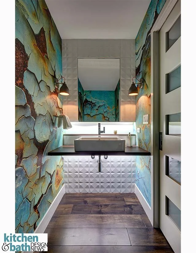 Modern bathroom with colorful abstract wall mural, floating black vanity with vessel sink, large mirror, exposed plumbing, wood flooring, and contemporary light fixtures.