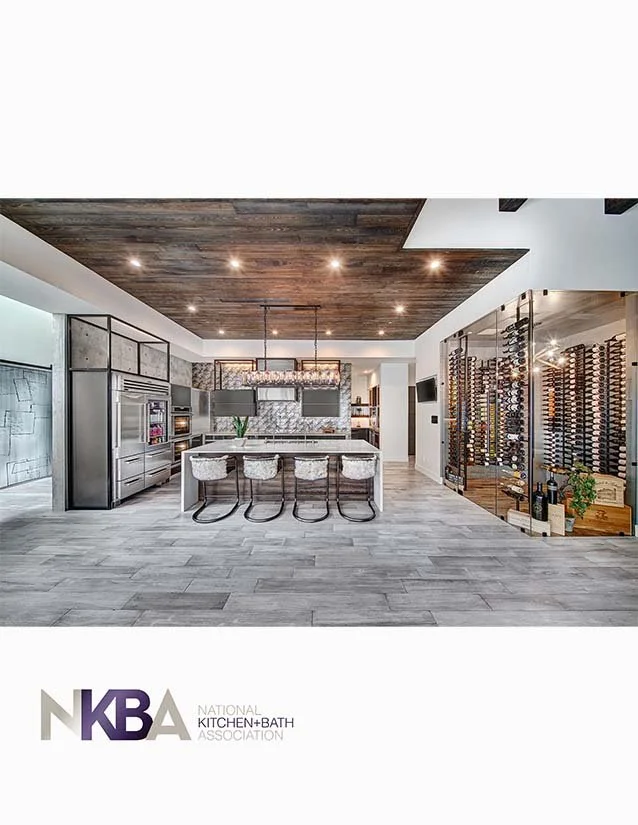 Modern kitchen with stainless steel appliances, white island with bar stools, wooden ceiling, and wine storage on the right.