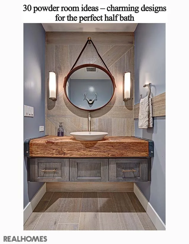 A modern half bathroom with a wooden vanity, vessel sink, round mirror, two vertical sconces, a towel holder, and decorative wall art, featuring a gray and beige tile design.
