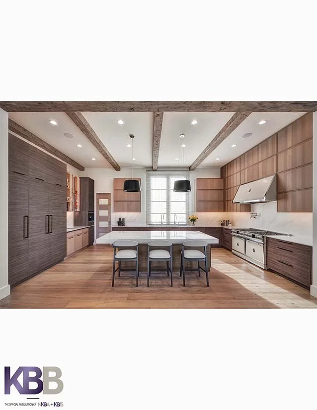 Modern open-concept kitchen with wooden cabinets, large island, black pendant lights, stainless steel appliances, and wooden flooring.