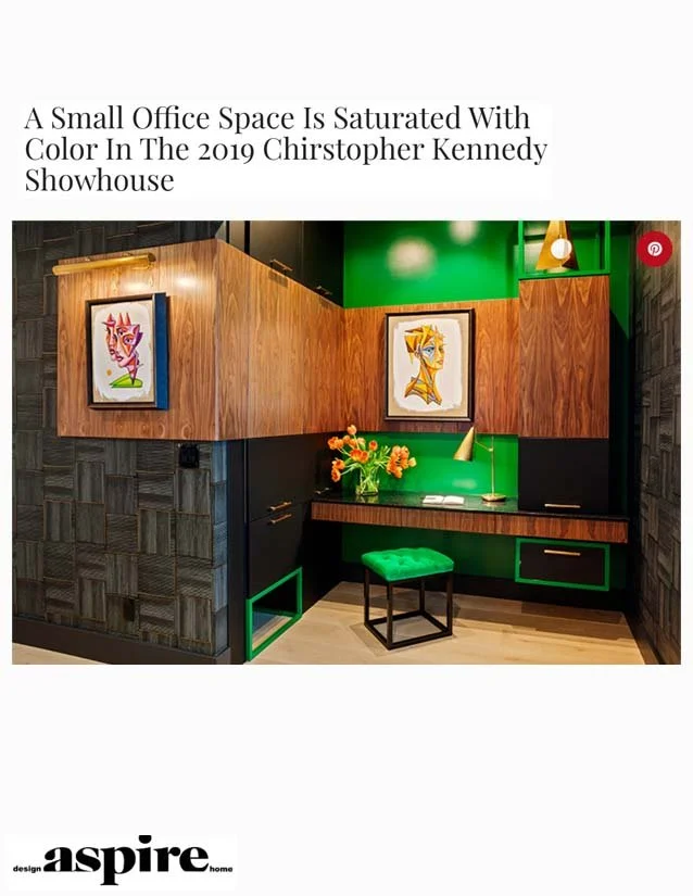 Small office space with wood paneling and green accents, featuring two colorful framed abstract art pieces, a green cushioned stool, a green lamp, and a vase with orange flowers.