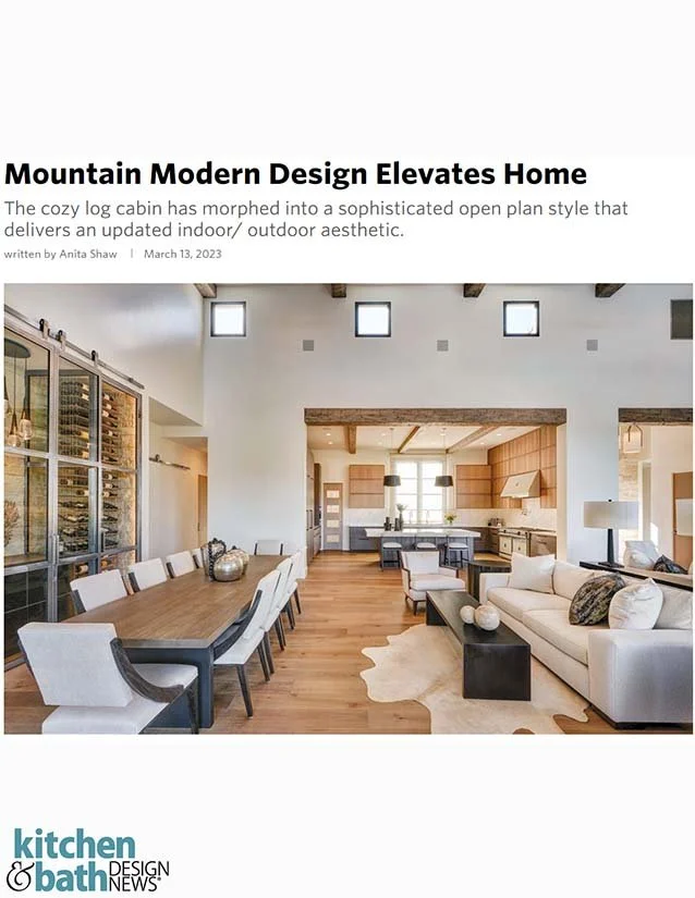Open concept living and dining area in a mountain modern home with wood flooring, large windows, a dining table with white chairs, a sofa with throw pillows, and a modern kitchen in the background.