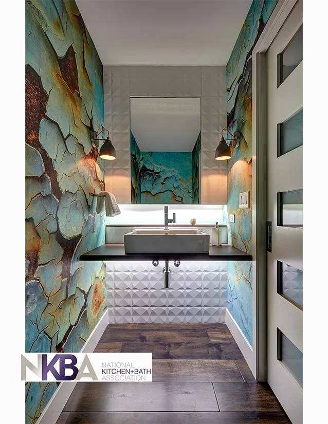 A small modern bathroom with colorful crackled art wall murals, a white vessel sink on a black countertop, and a large mirror reflecting more of the mural, with wood flooring.