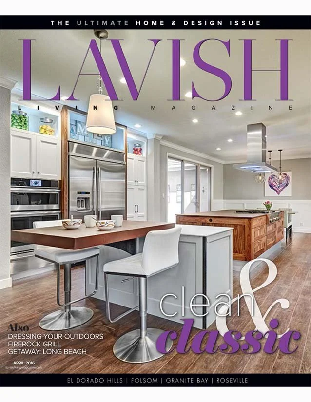 Cover of Lavish Living Magazine featuring a bright, modern kitchen with white cabinets, stainless steel appliances, a wooden island, and a dining area with bar stools. The title reads "LAVISH" in large purple letters, with the subtitle "clean & class