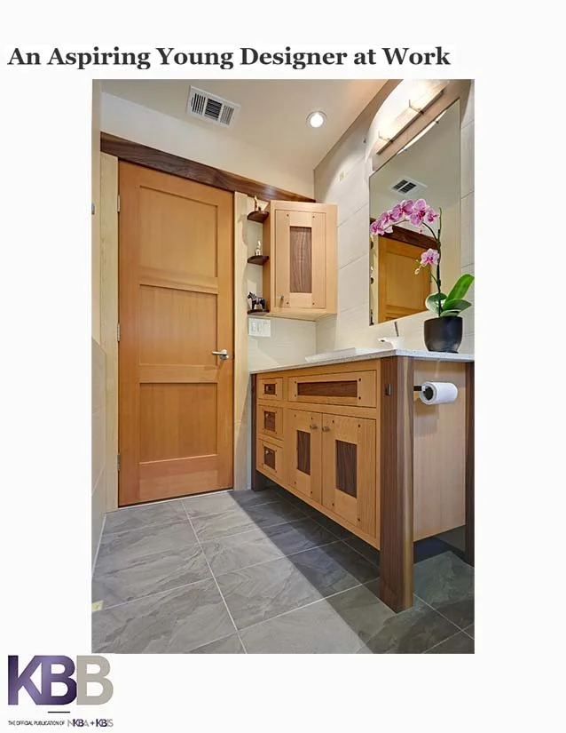 A modern bathroom vanity with wooden cabinetry, a large mirror, and pink orchids on the countertop. There is a wooden door to the left and a wall-mounted cabinet. The floor is tiled, and the space appears to be well-lit.