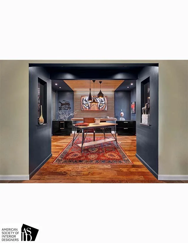 Interior view of a room framed by dark walls, featuring a wooden dining table, a colorful Persian rug, and modern art on the back wall.