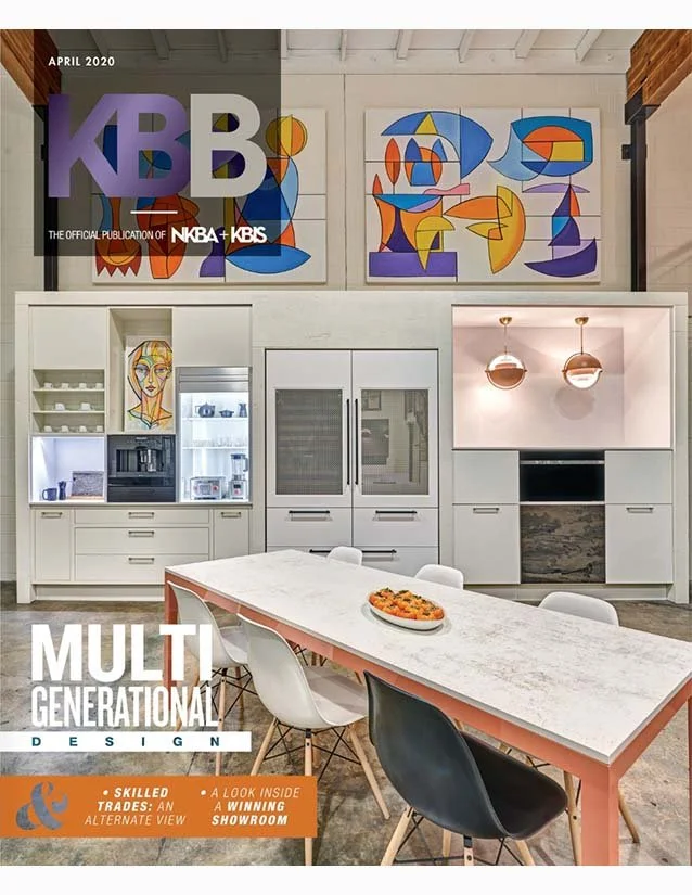 Modern kitchen with white cabinetry and colorful abstract artwork on the wall, a kitchen island with chairs, and a magazine cover with headlines about multi-generational design.