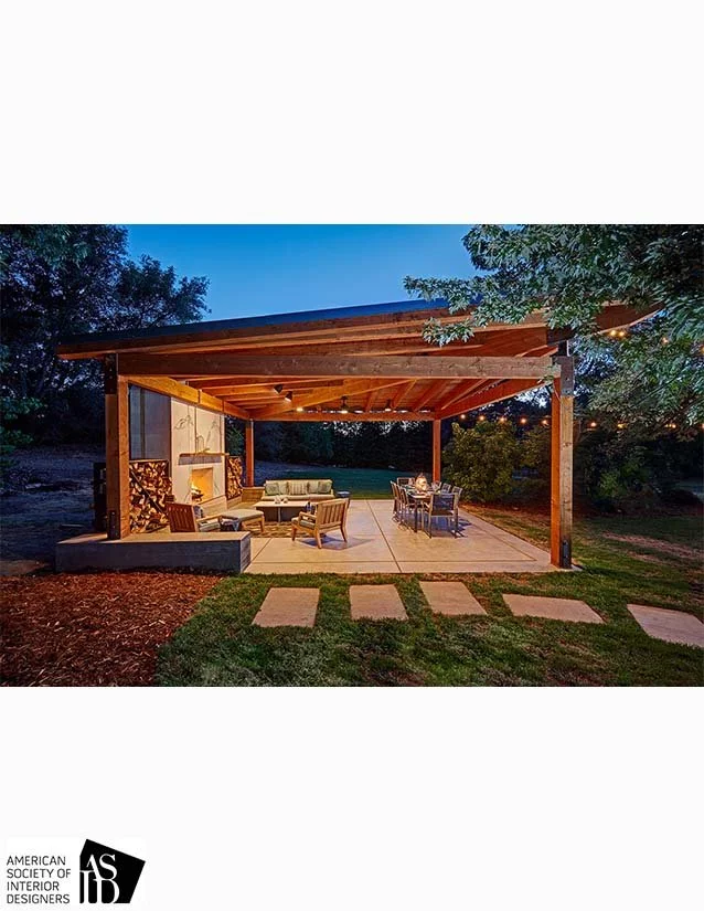 Outdoor patio with seating and dining area under a wooden pergola, surrounded by trees at dusk.