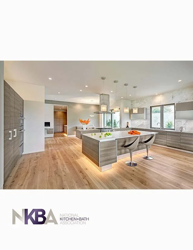 Modern kitchen with light-colored wood flooring, gray cabinets, a large central island, pendant lighting, and windows with natural light.