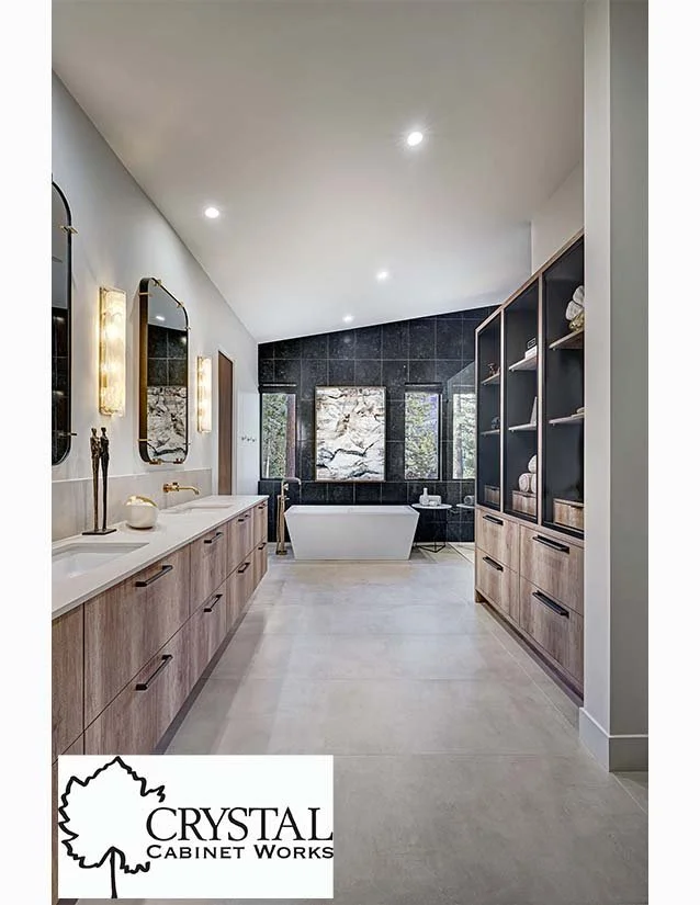 Modern bathroom with a freestanding bathtub, black tiled accent wall, and large windows, with wooden cabinetry and decor.