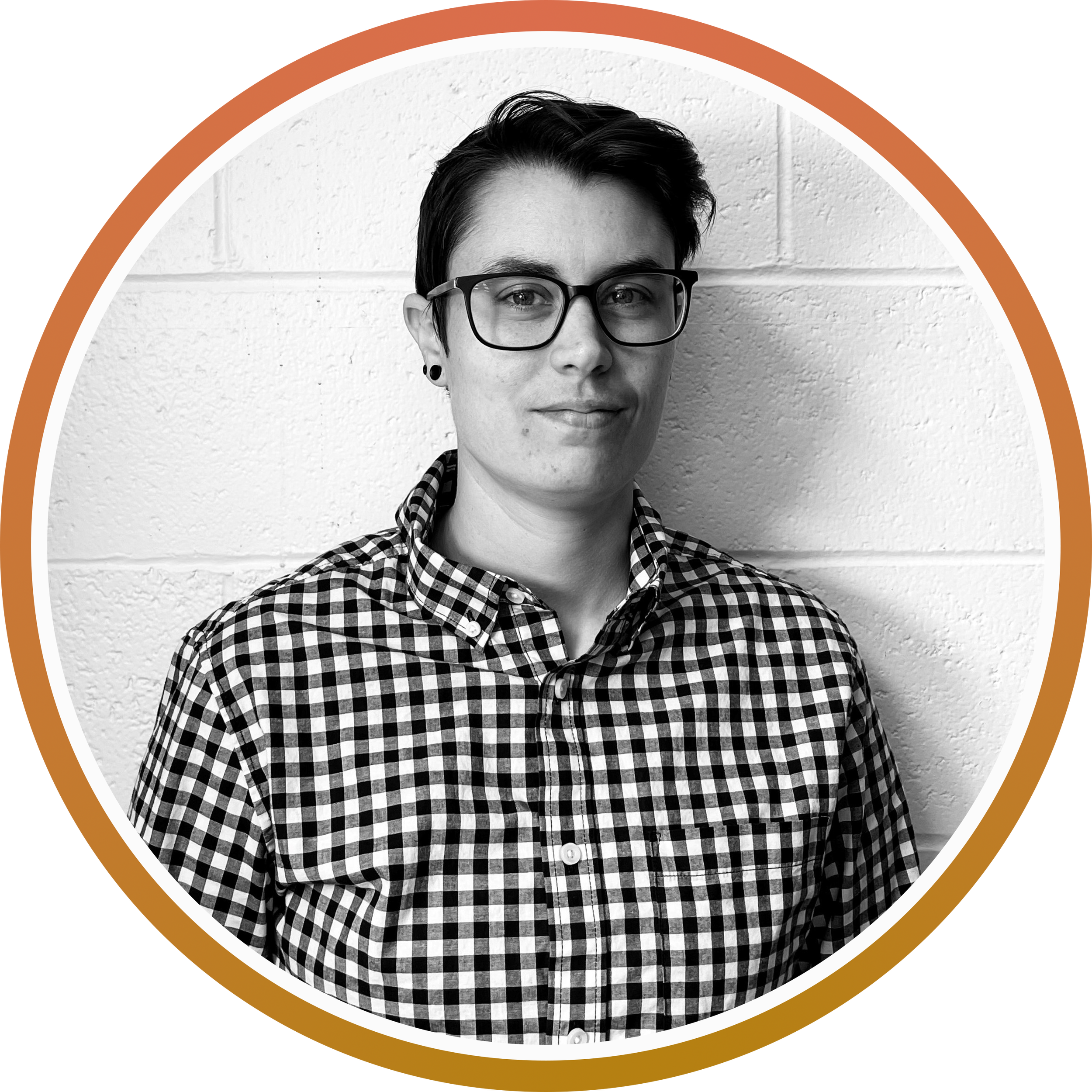 Black and white portrait of a person with short dark hair, glasses, and a checkered shirt, standing against a textured wall.