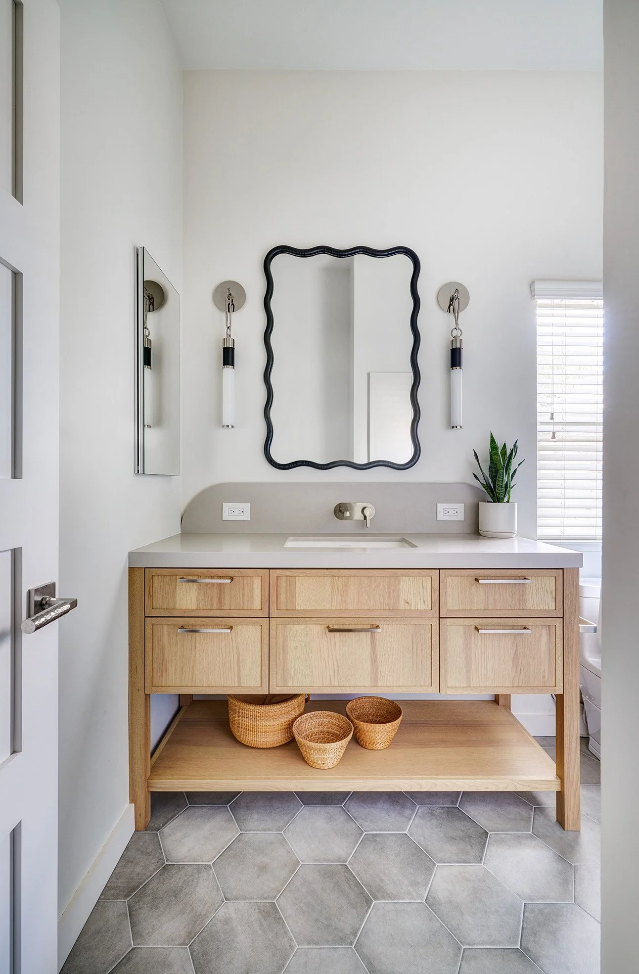 Wood bath vanity with open legwork and shelf, decorative mirror and sconces and recessed medicine cabinet.