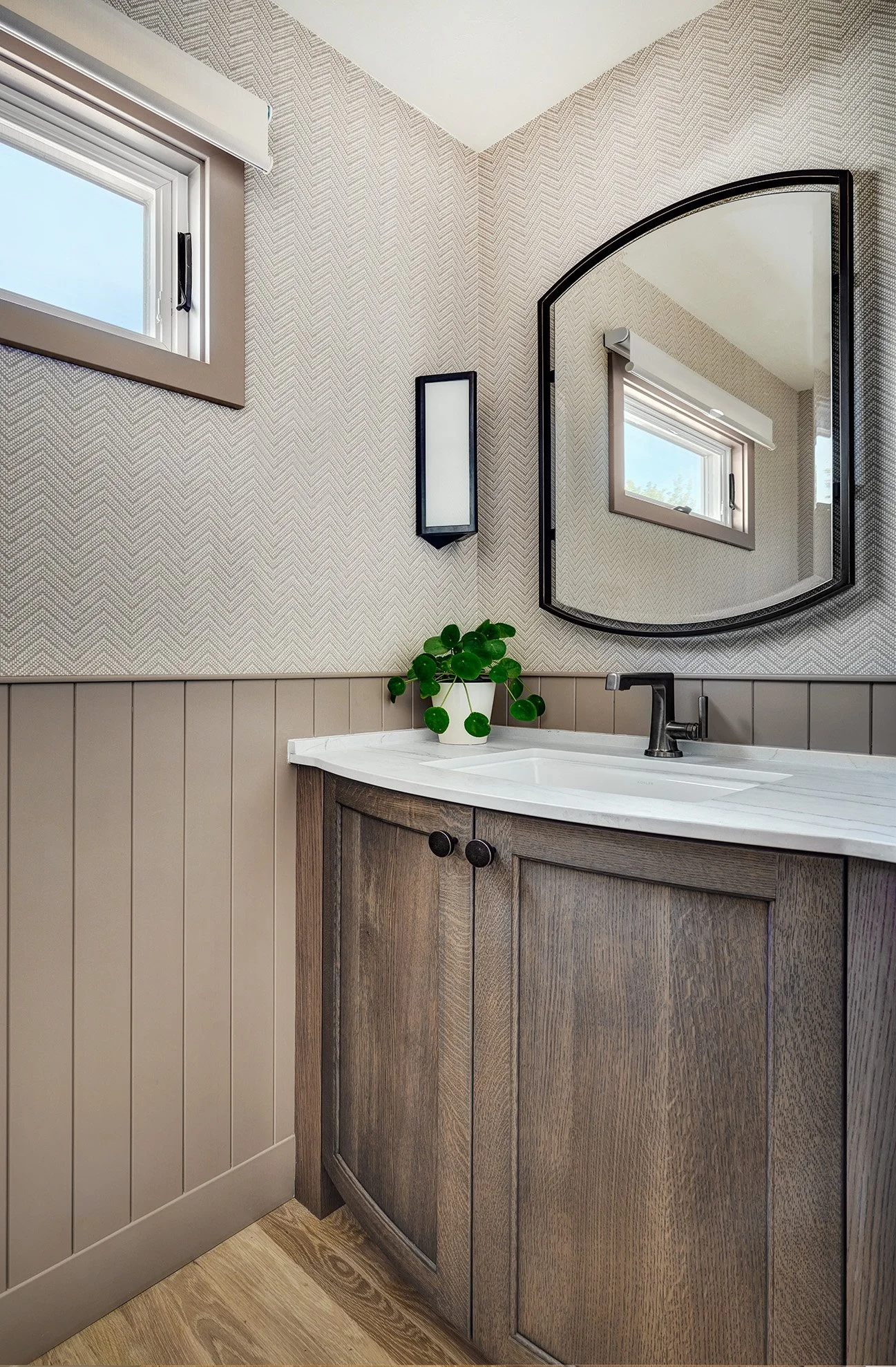 Warm bowed front vanity cabinetry in powder bathroom, wallpaper and warm taupe wainscot 